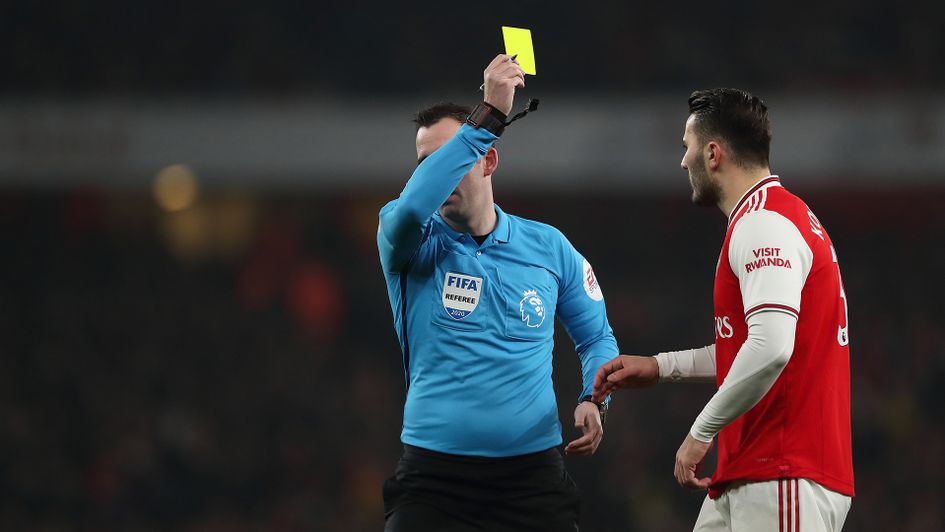 Chris Kavanagh shows a yellow card to Sead Kolasinac